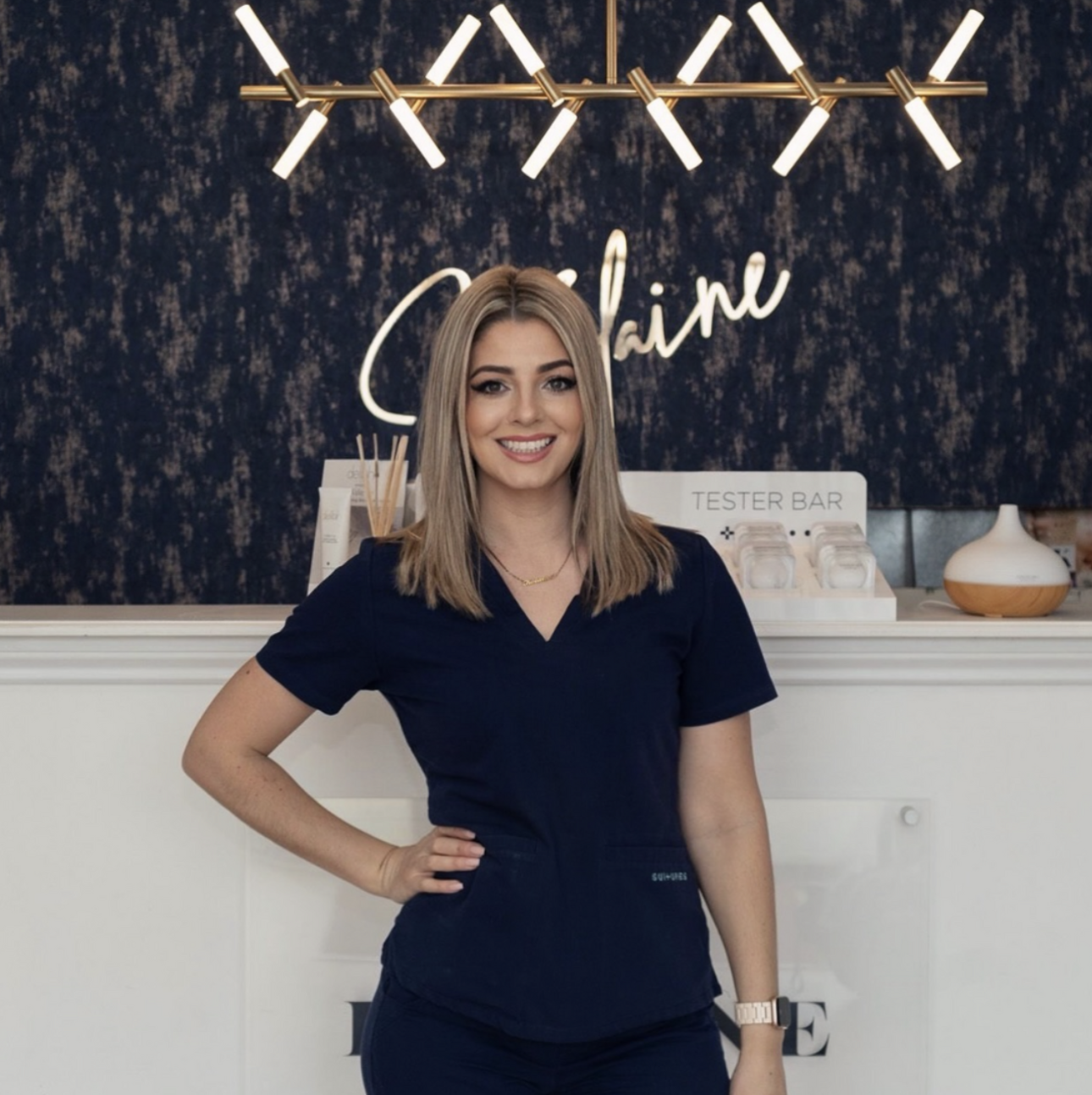 Kolaine Farr, founder of Kolaine Beauty Lounge, standing confidently in the clinic reception area wearing a navy uniform.